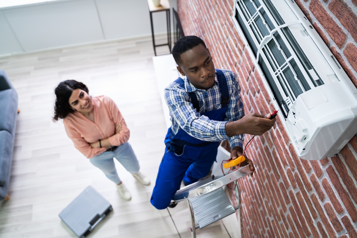 Woman Looking At Technician Repairing Air Conditioner