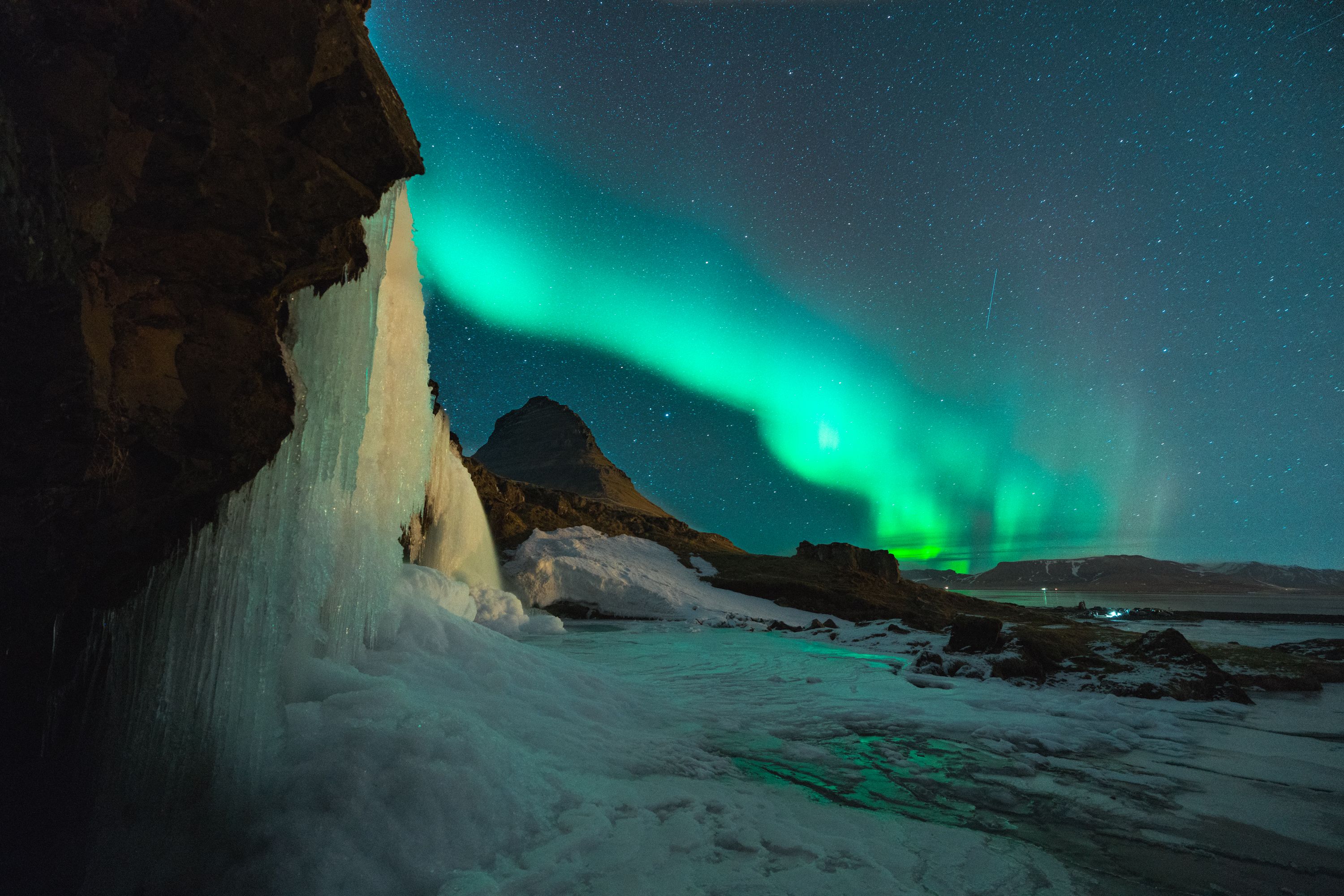 Northern Lights glow above Iceland's Kirkjufell mountain and frozen waterfall.
