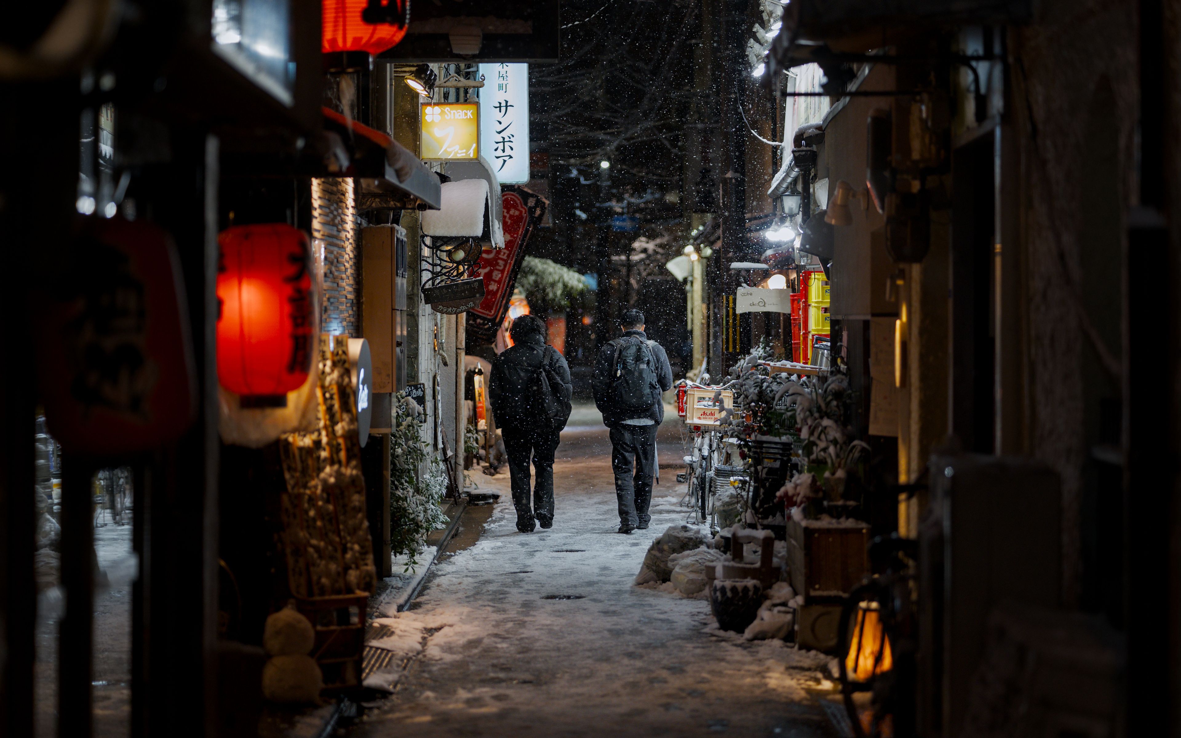 Snow settles on a Kyoto alley as traditional lanterns glow at night, evoking a winter trip to Japan.