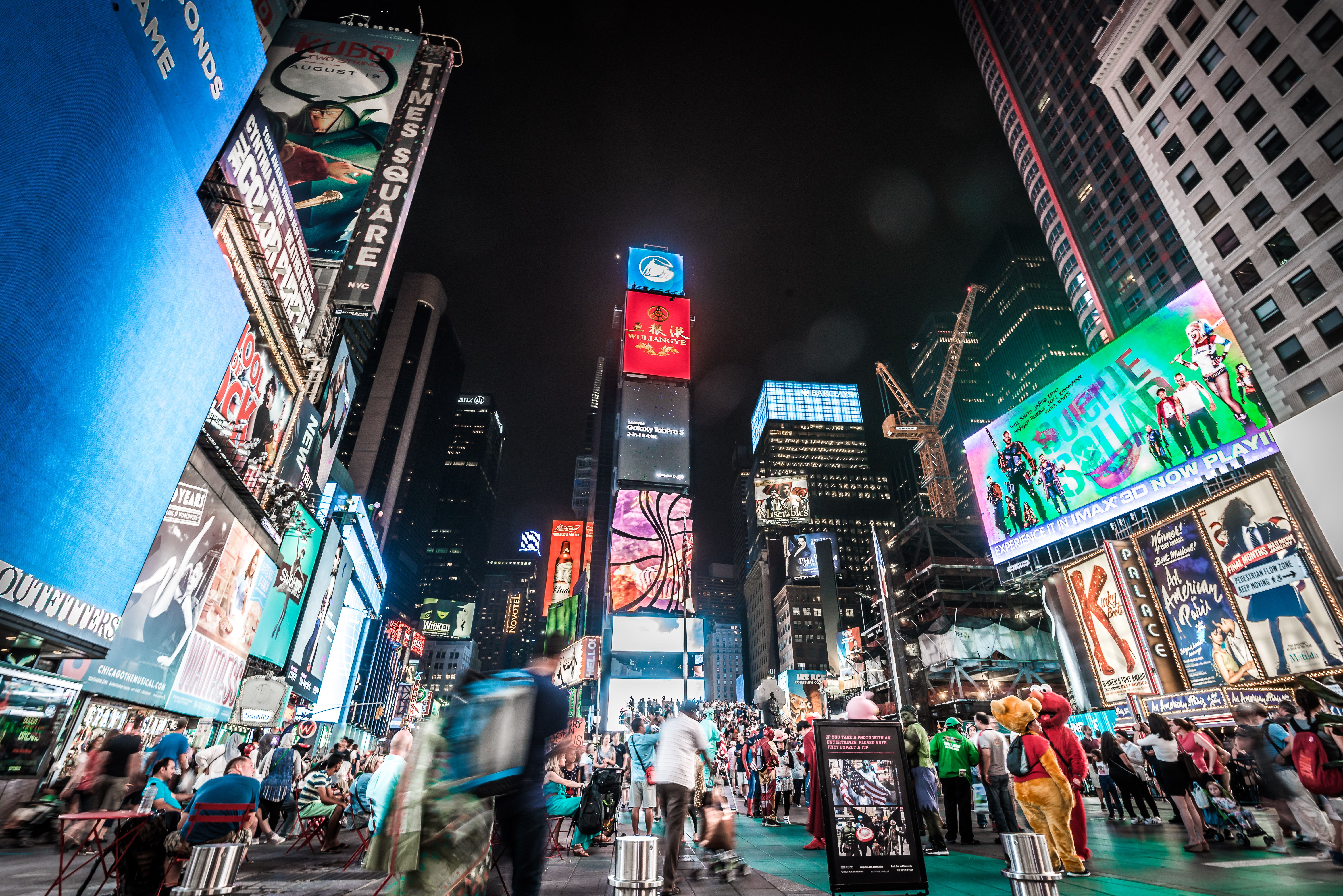 Times Square crowds and towering digital billboards illuminate New York City at night.